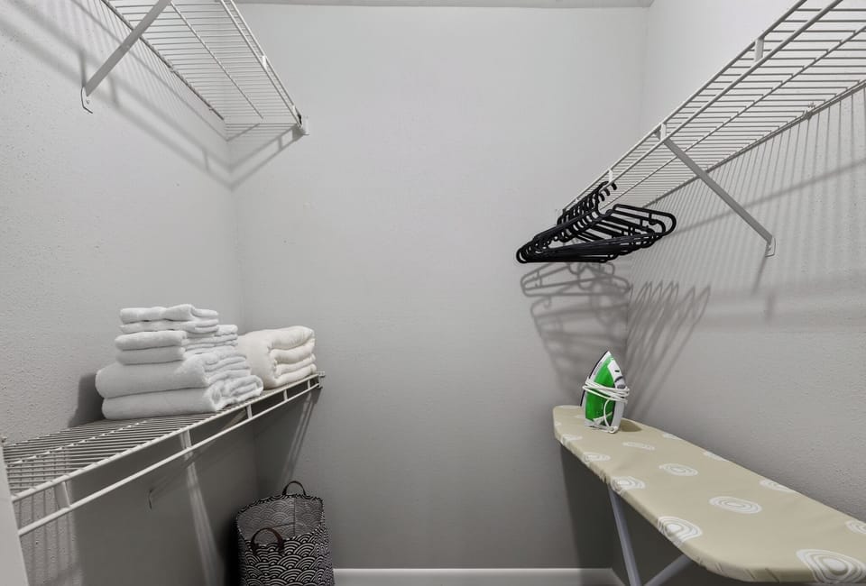 Spacious walk-in closet with fresh towels, hangers, hamper, iron & ironing board