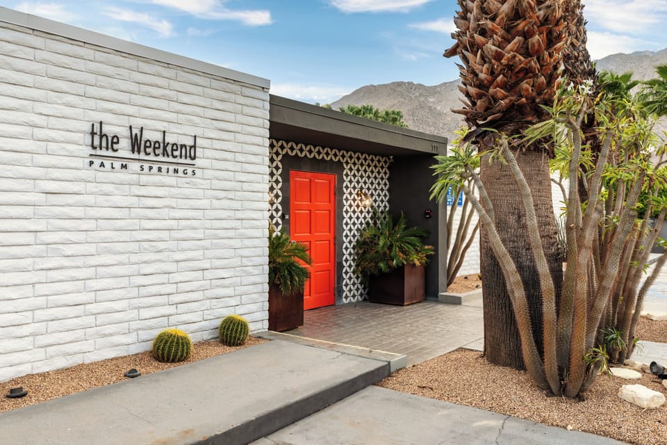 Welcoming property entrance featuring a signature bright orange door and lush desert landscaping.