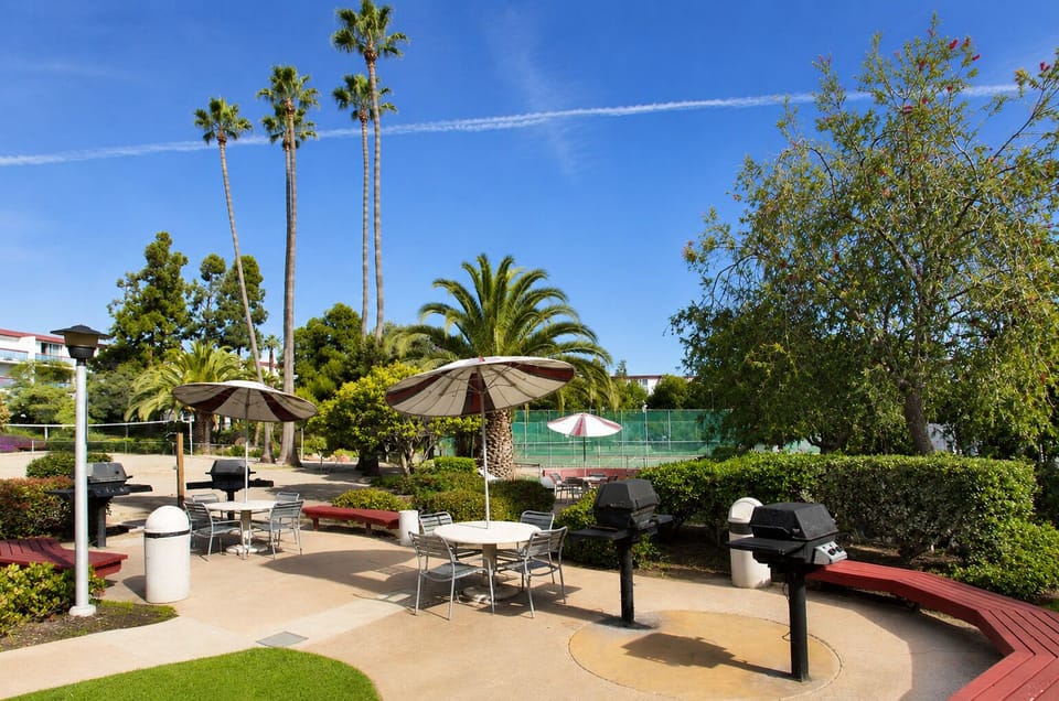 Sunny resort-style BBQ patio with shaded seating and tennis court access