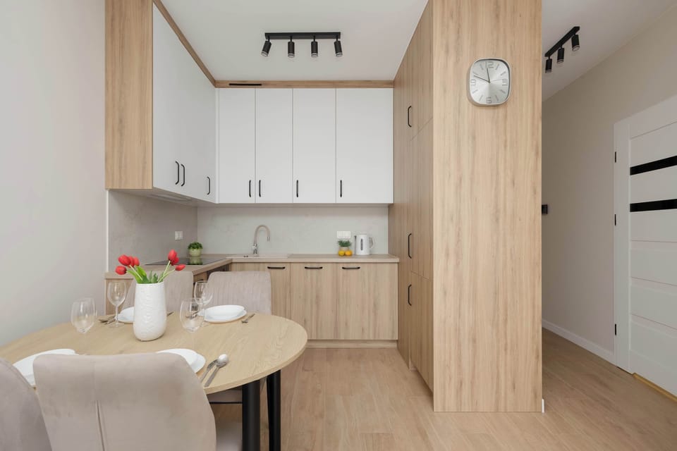 A dining nook includes a round wooden table paired with upholstered chairs. The kitchen cabinets and an entrance door frame the background.