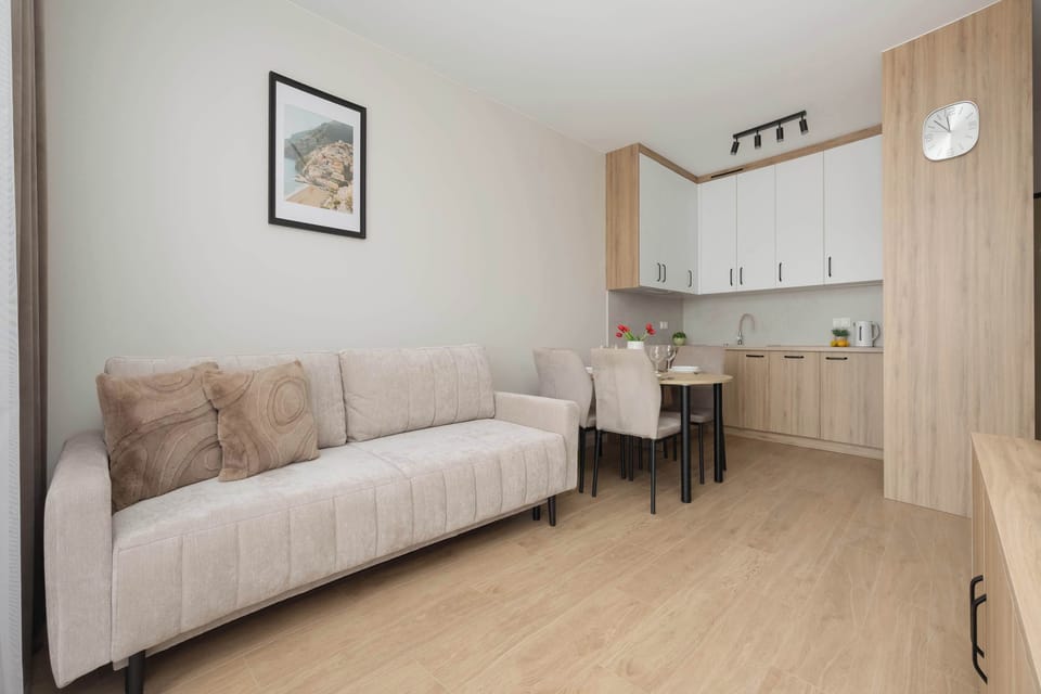 An open-plan view shows the beige sofa positioned next to a small dining area. The kitchenette lines the background of the apartment layout.