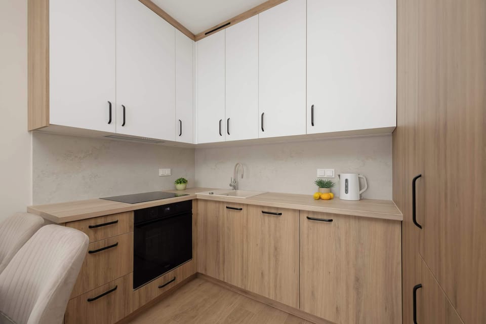 A corner kitchenette combines white upper cabinets with light wood-grained lower units. Built-in appliances include a black induction cooktop and oven.