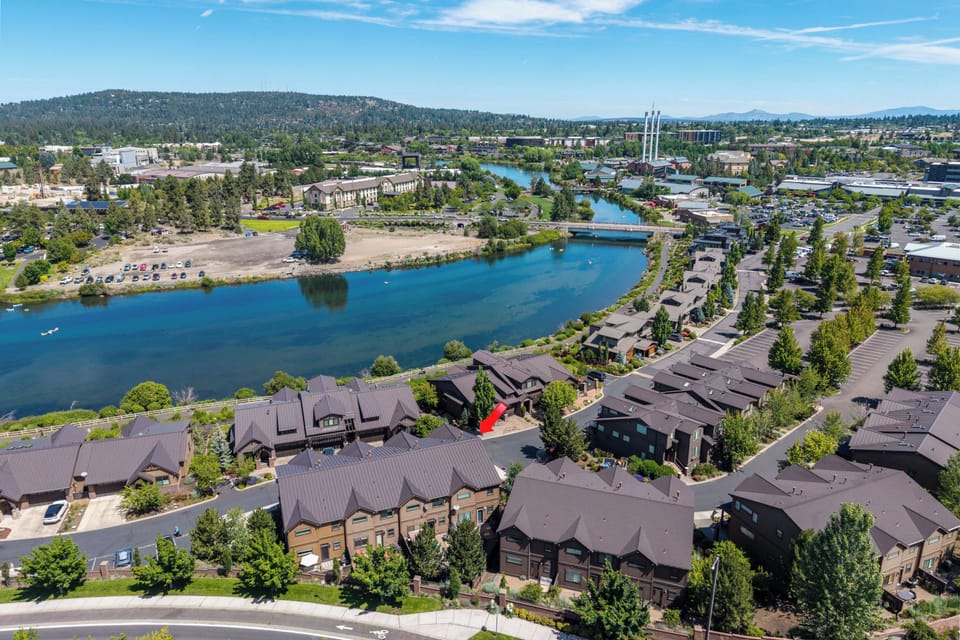 Aerial view of the vacation rental property situated along a scenic river in a peaceful residential community, surrounded by natural landscapes and nearby mountains.
