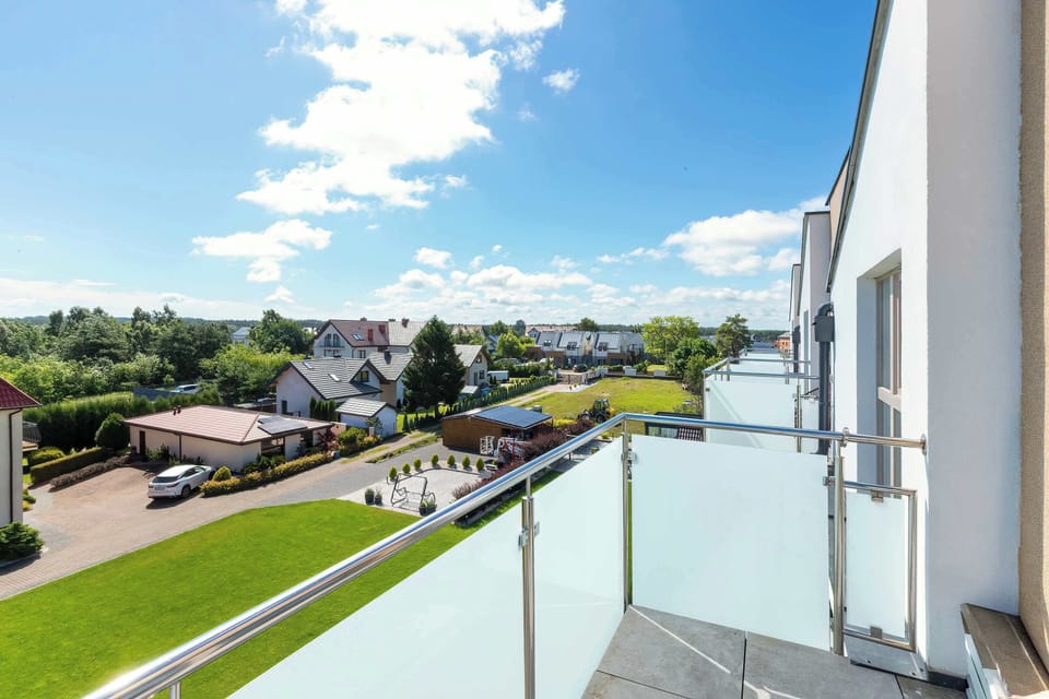 The high-angle view from a balcony captures surrounding green lawns and a paved driveway below. A clear blue sky opens up over the neighborhood.