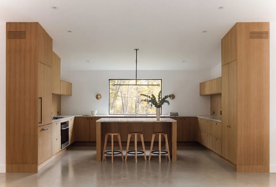 Chef's kitchen in white oak with a stone island, counter seating, and a forest view.