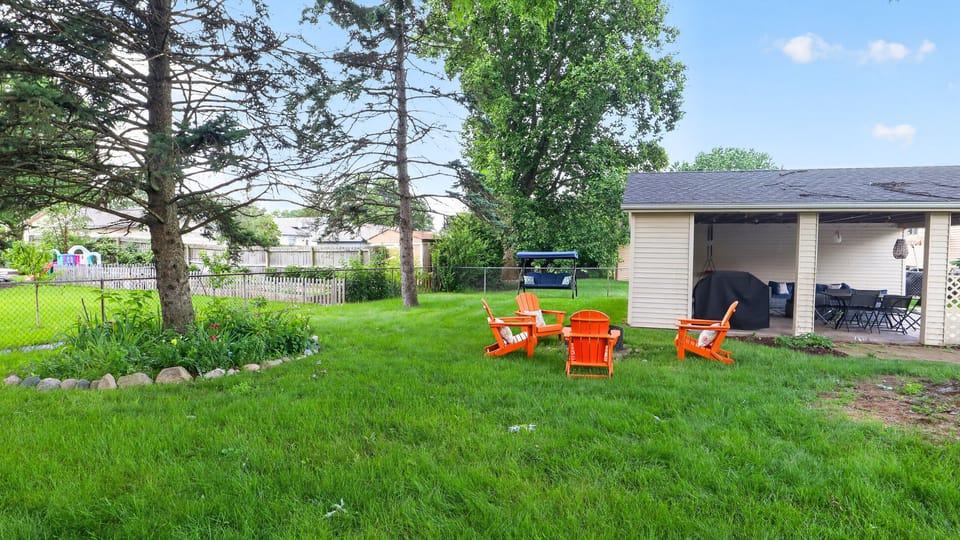 Flat, grassy backyard with a fire pit, glider swing, and room to relax or play.