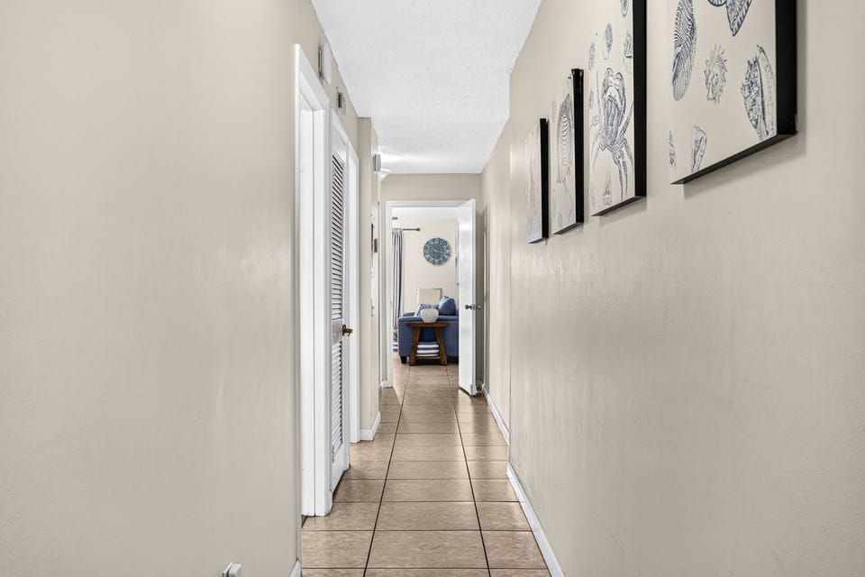 Bright tiled hallway with coastal decor leading to a cozy bedroom