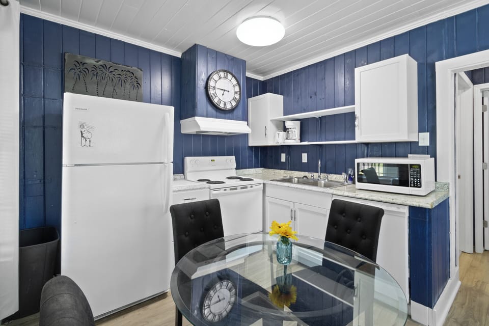 Prepare family meals in the bright, full kitchen featuring bold blue paneled walls, white cabinetry, and a modern glass-top dining table.