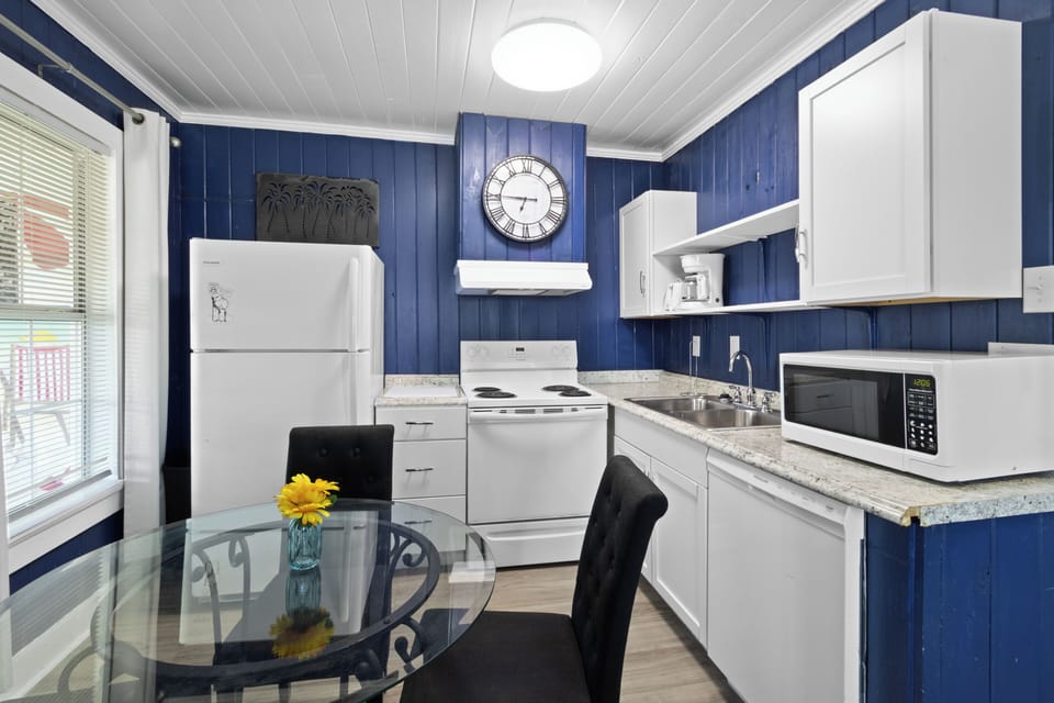 Enjoy home-cooked meals in the fully equipped kitchen, which includes a glass-top dining table, standard appliances, and crisp white cabinetry.