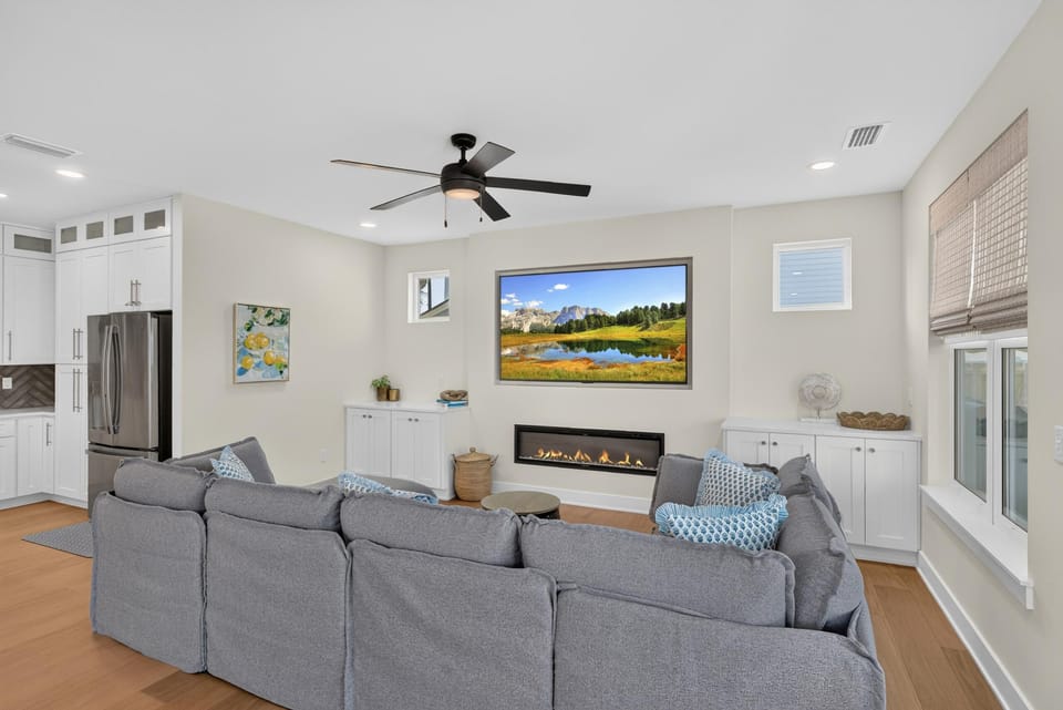 Living room features a gray sectional with patterned pillows, a linear fireplace, and a landscape TV above built-in white cabinets.