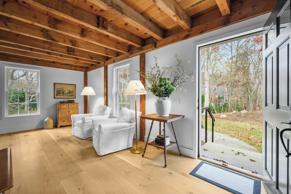 Bright entry lounge with exposed beams, cozy seating, and wooded views