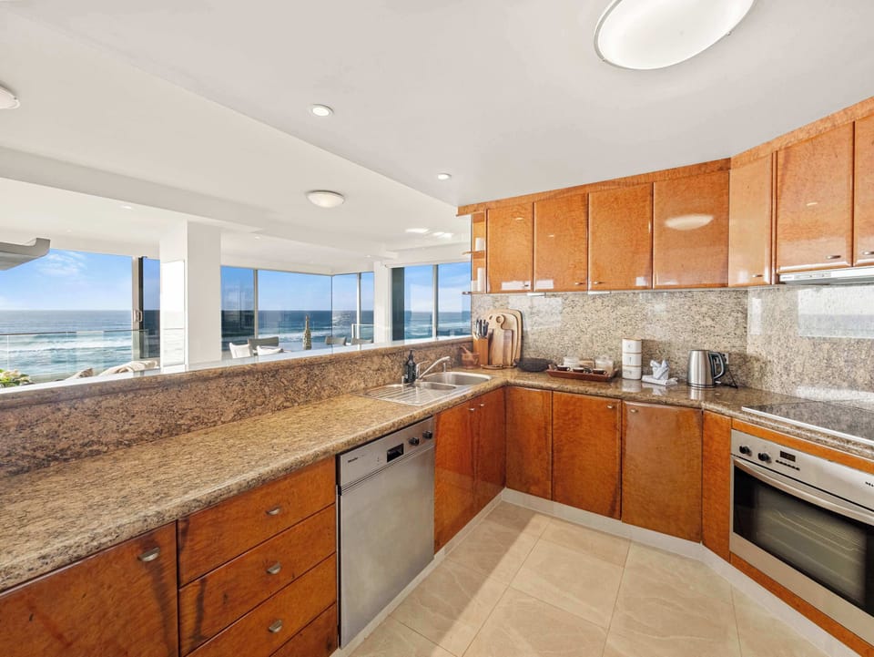 The kitchen in granite and timber, Miele throughout, the sea over the sink.