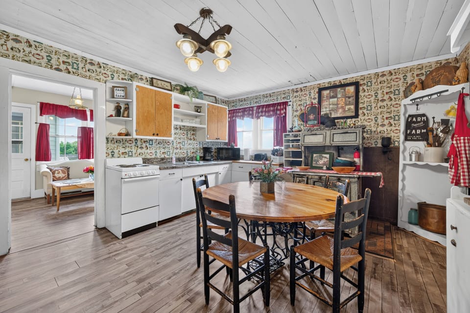 A rustic, farm-style kitchen and dining area with vintage wallpaper and a wooden table.