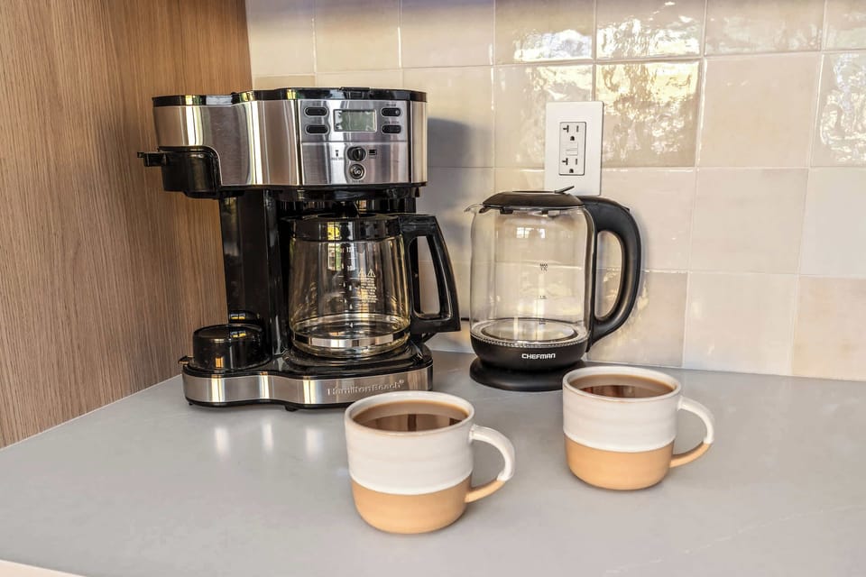 Drip coffee maker, electric kettle and mugs provided.