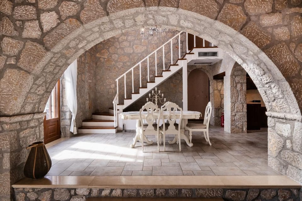 Stone archway framing an elegant white dining table and rustic staircase.