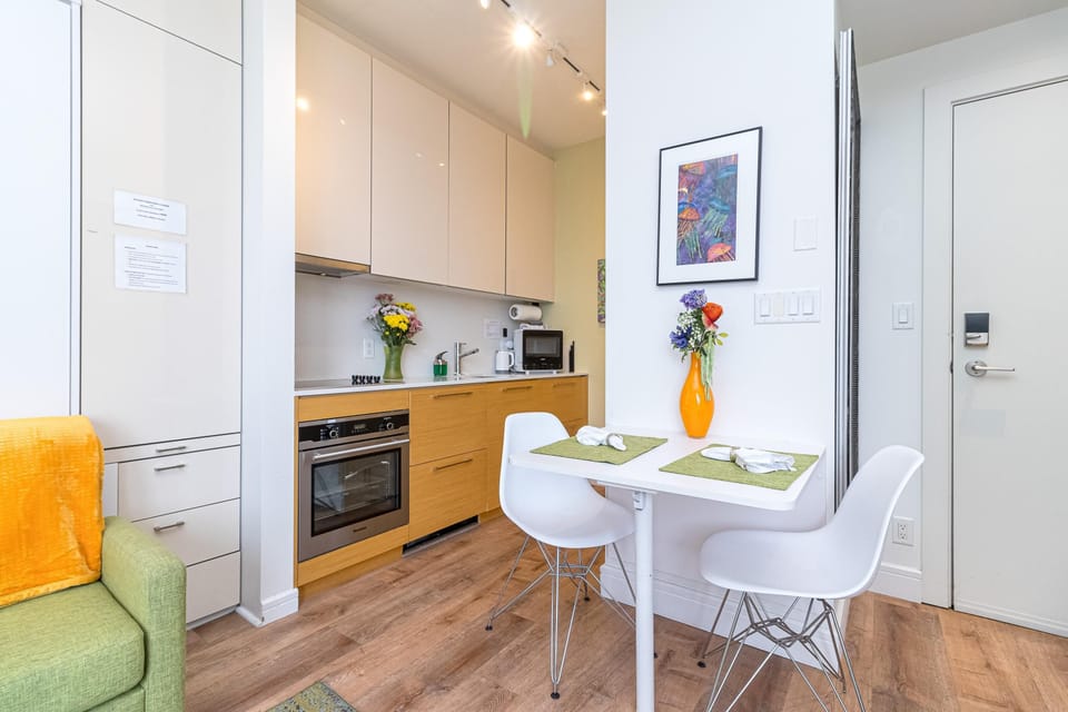 Compact dining nook with white table, modern chairs, and an orange vase of flowers against white walls.