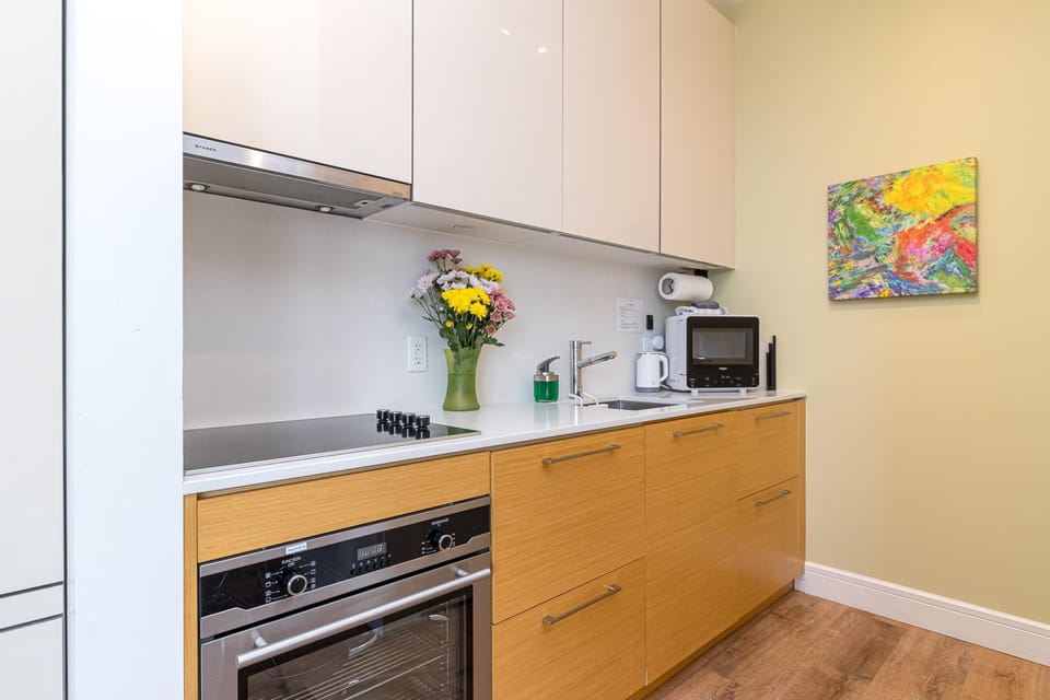 Light wood lower cabinets contrast with glossy white uppers in the kitchen, featuring stainless appliances and colorful wall art.