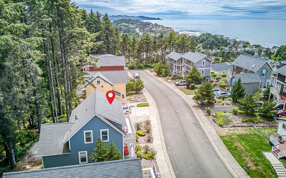 Aerial view of coastal neighborhood homes with ocean and mountain vistas visible in the distance, marking the property's scenic hillside location.