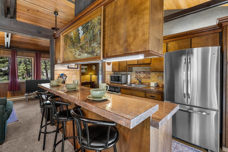 Picture yourself preparing meals in this inviting open-concept kitchen, where warm wood tones and modern appliances meet cozy mountain charm, and breakfast at the island overlooks scenic forest views.