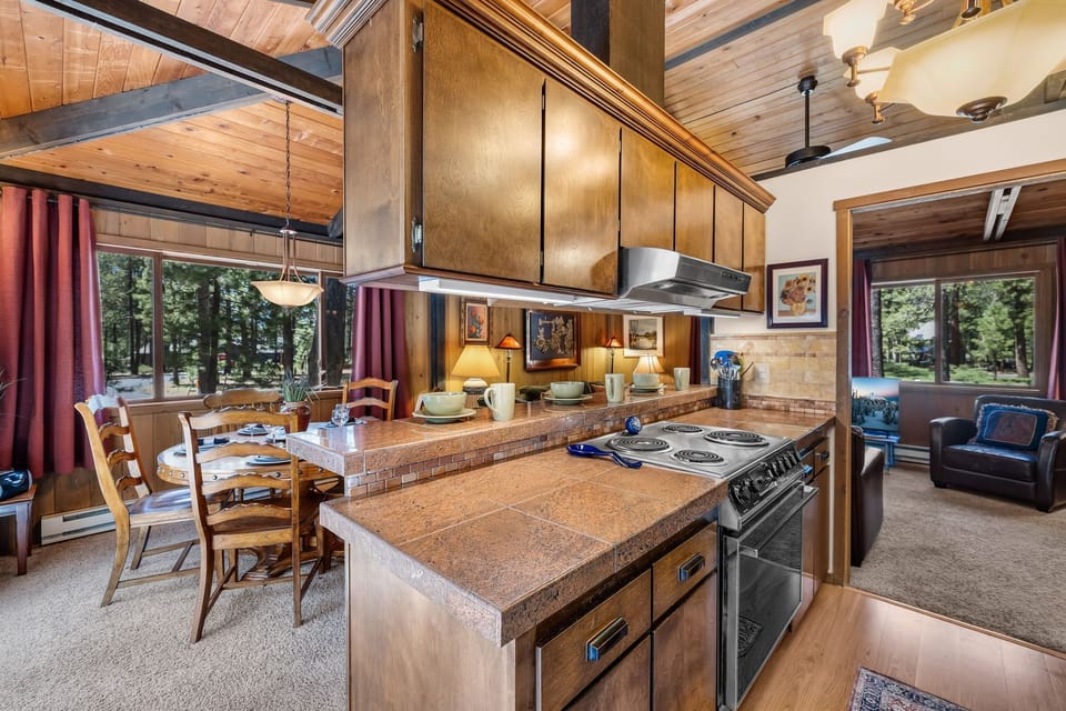 Warm wooden beams frame your open-concept kitchen and dining space, where natural light pours through forest views. Cook meals on the full range, gather at the dining table, then unwind in the cozy living nook.