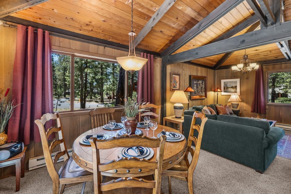 Settle into your cozy retreat where vaulted wood ceilings and natural light create a warm, inviting atmosphere. The dining table is set for memorable meals, while forest views through large windows bring the outdoors in.