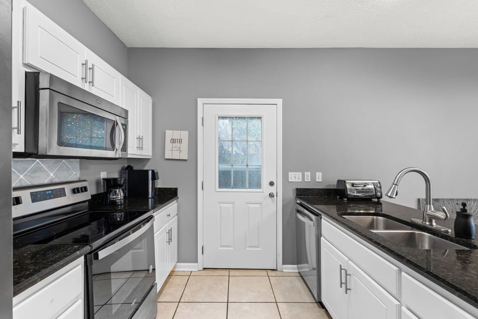 You'll love preparing meals in this bright, fully equipped kitchen with sleek white cabinetry, granite countertops, stainless appliances, and plenty of space to gather with loved ones.