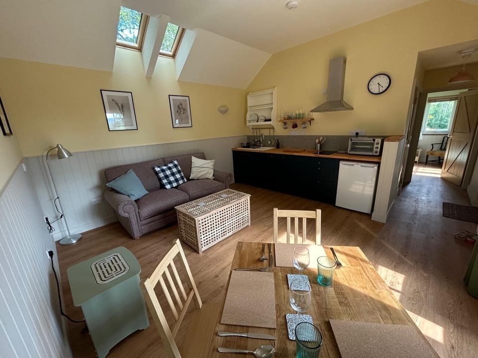 No. 3
Bright living area and kitchen featuring two Velux windows with blackout blinds for restful sleep when using the comfortable double sofa bed. The space includes an Everhot electric stove with an integrated warming oven, and double French doors opening onto private decking. The modern kitchen comes with a 10-in-1 combi oven, two-burner induction hob, fridge-freezer, and half-size dishwasher. Eco-friendly supplies include Smol dishwasher tablets and Miniml dish soap, complemented by biodegradable scourers and washable dishcloths.