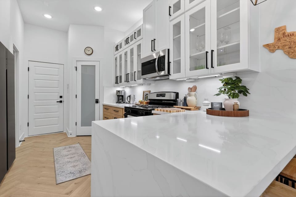 Sleek kitchen with quartz peninsula, gas range, coffee nook, glass cabinets.