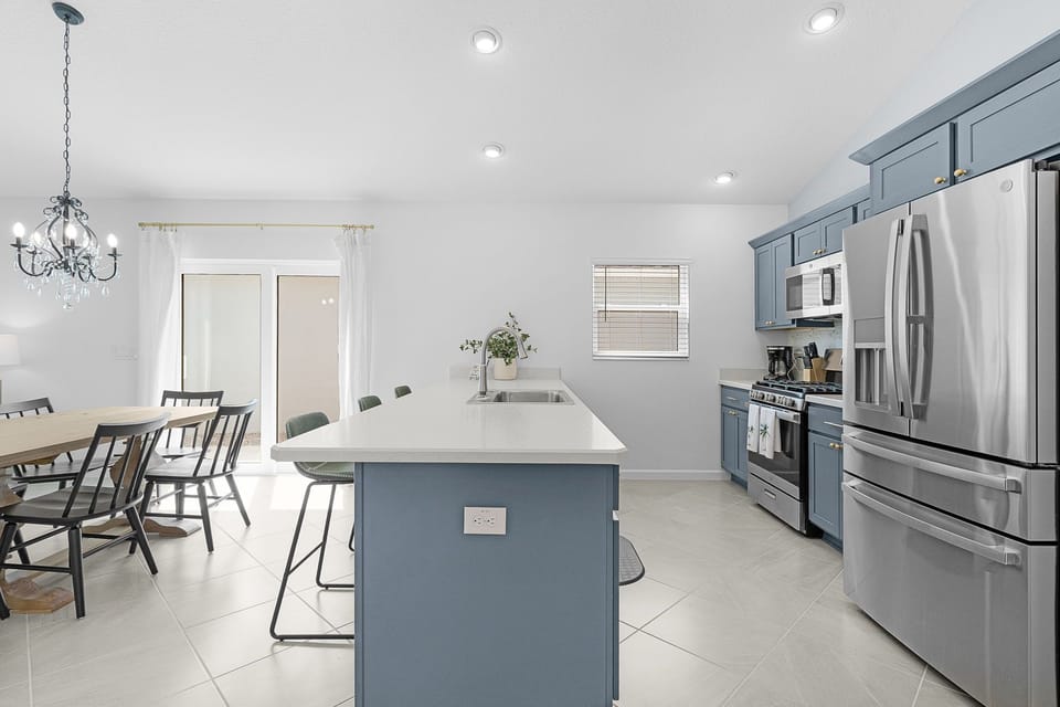 Gather around the sleek island in your fully-equipped kitchen, where blue cabinets and stainless-steel appliances make meal prep a breeze. Natural light floods the open dining space, creating a welcoming spot for shared meals.