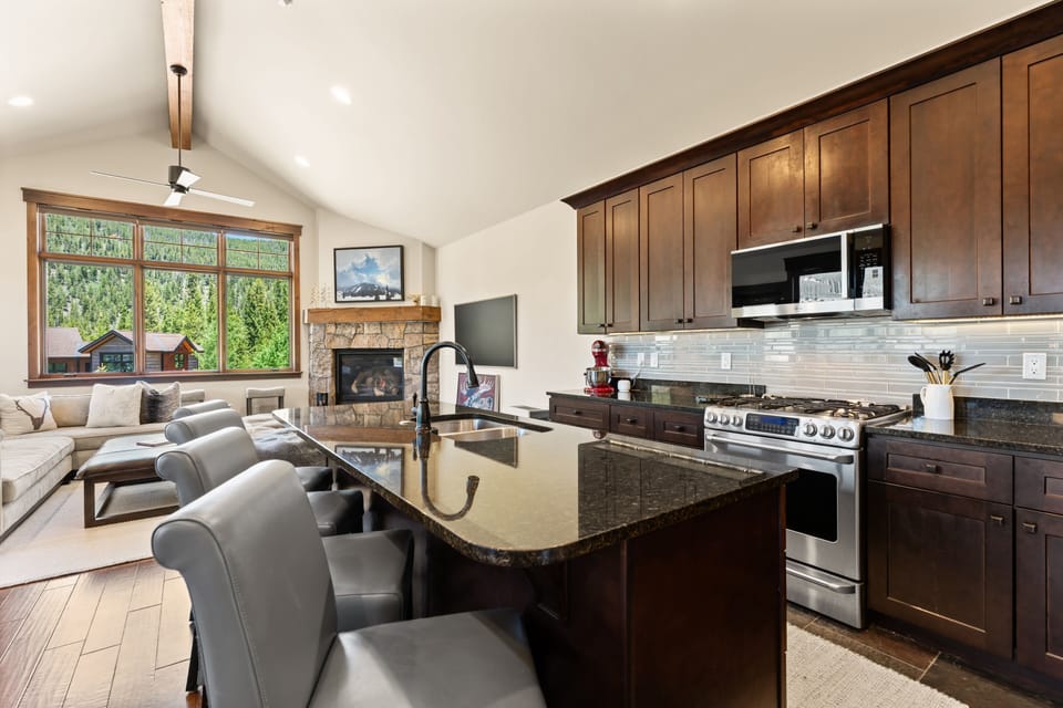 Your open-concept haven blends warmth and function, with a chef's kitchen flowing into a cozy living space framed by mountain views and a stone fireplace.
