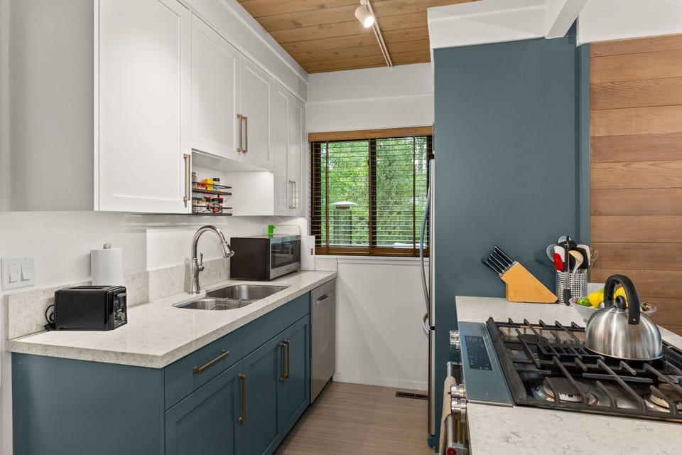 Stylish modern kitchen with gas range, stone counters, and forest views