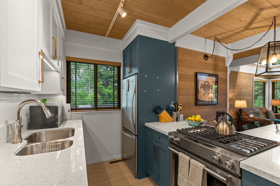 Bright designer kitchen with gas range, quartz counters, and forest views