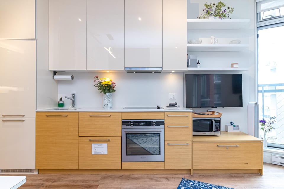 Light wood lower cabinets contrast with glossy white upper storage, surrounding a stainless steel oven and cooktop.