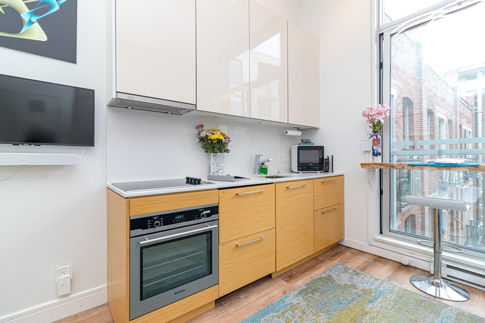 Kitchen features light wood lower cabinets, glossy white upper cabinets, and a compact electric stovetop.