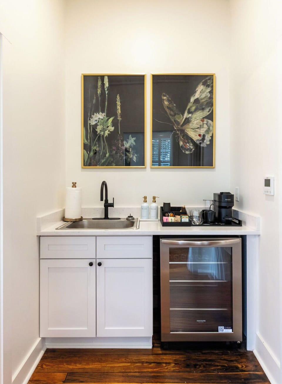 Chic coffee bar with mini fridge, sink, and elegant botanical artwork