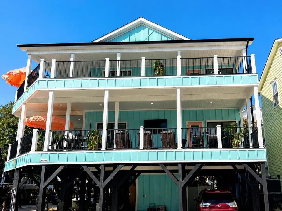 Two-story wraparound balcony with black metal railings, cushioned wicker chairs, and coral scalloped umbrellas.