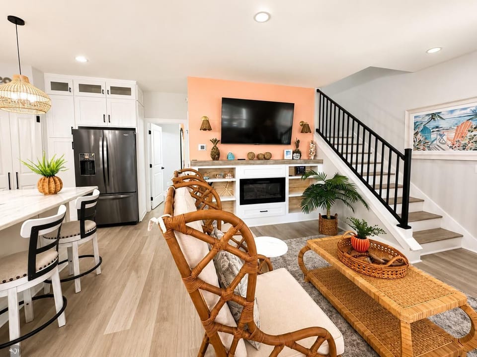 Open living area with rattan armchairs, woven coffee table, wall-mounted TV over a white fireplace mantel.