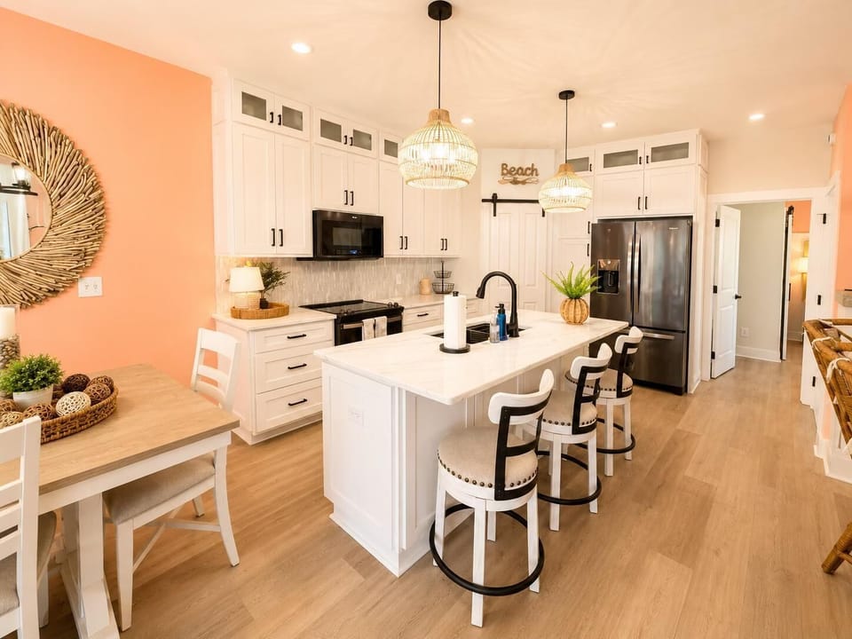 Kitchen with marble island, black faucet, three cushioned bar stools, white cabinetry, and peach accent walls.