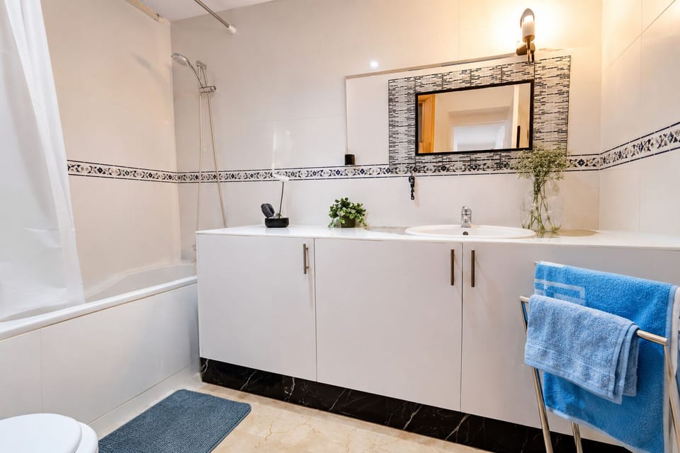 Modern bathroom with bathtub, large mirror, vanity storage, and fresh towels.