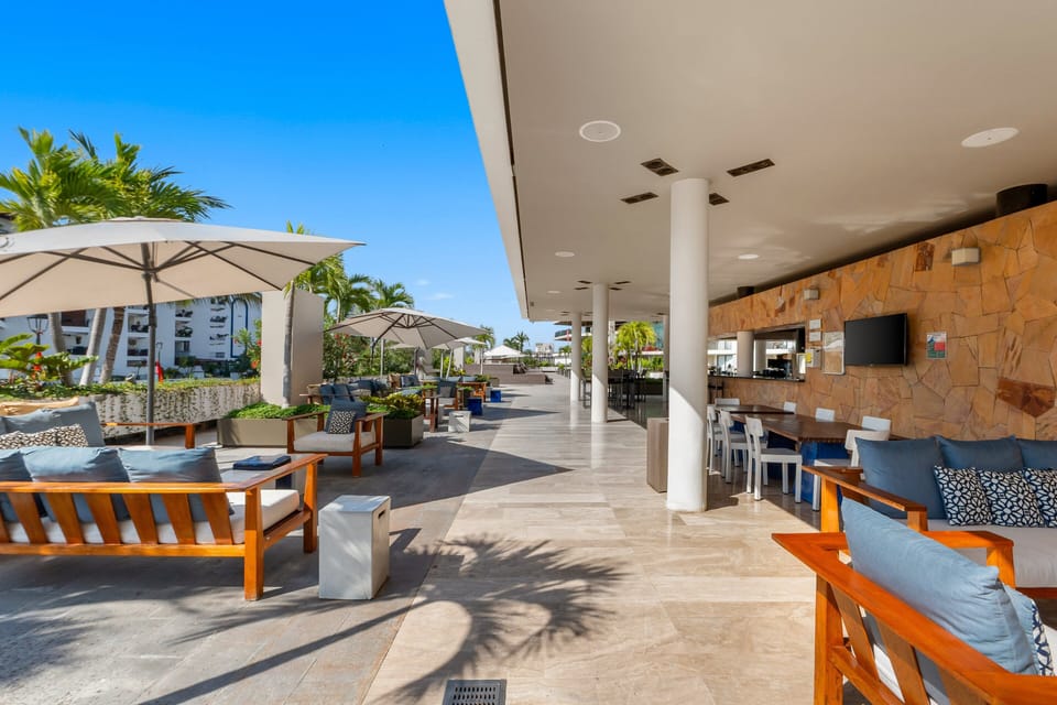 This upscale patio features stylish wooden sofas with plush cushions, large umbrellas, and an adjoining covered bar area perfect for social gatherings.