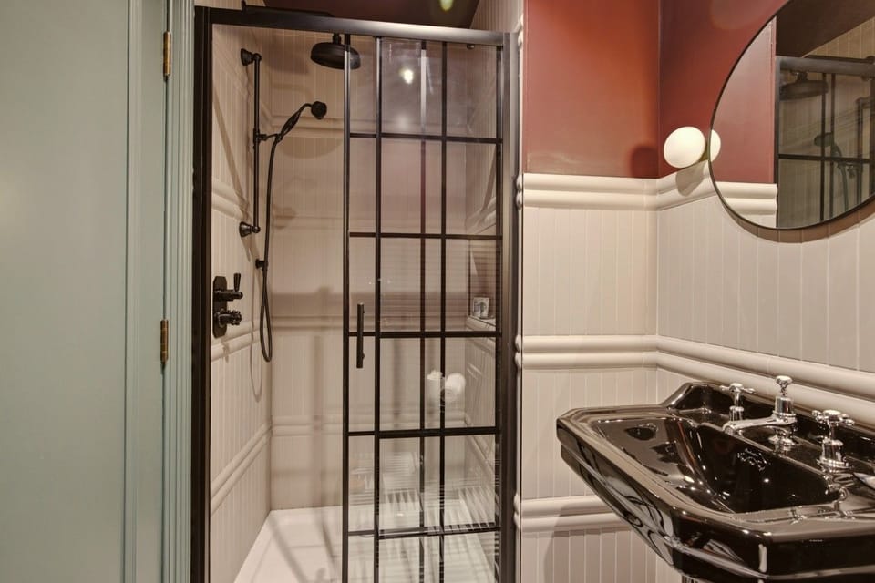 Modern shower room with walk-in shower, black basin and round mirror.