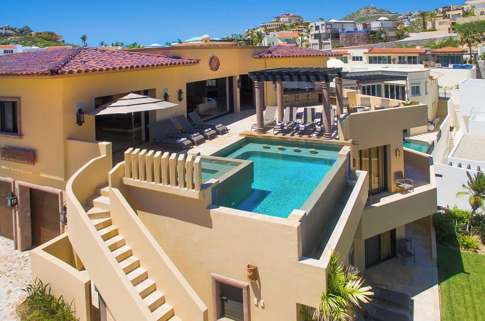 A luxurious hillside villa featuring a private rooftop pool with lounge chairs and shaded cabana, set against scenic neighborhood views and clear blue skies.