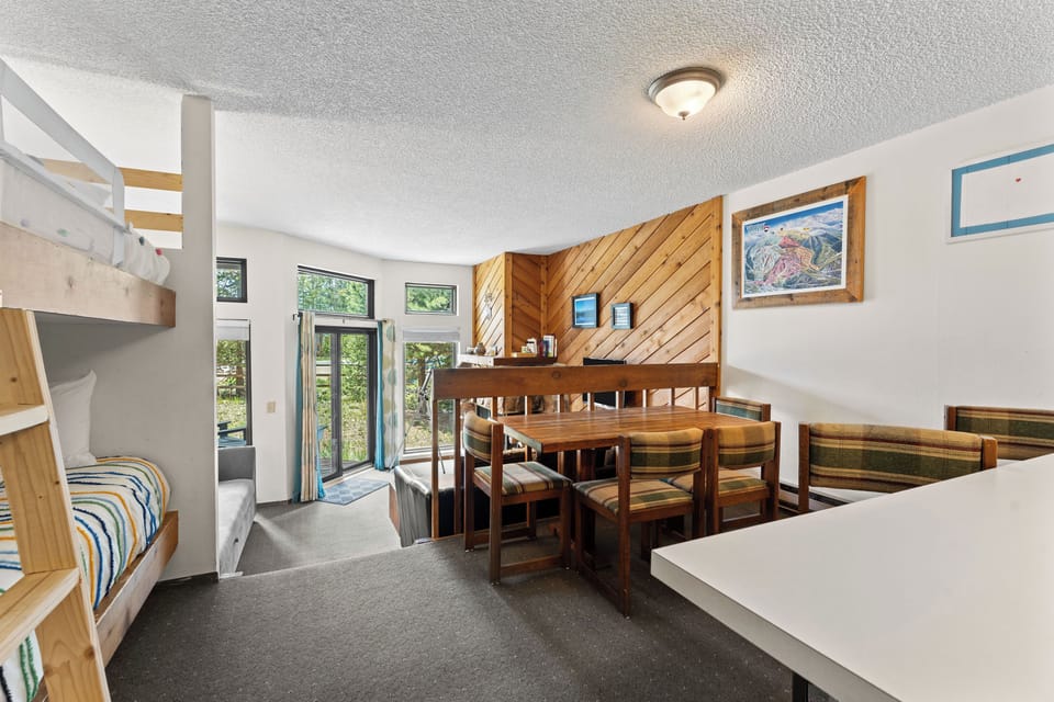 Your group's cozy retreat features handcrafted woodwork, bunk sleeping areas, and a welcoming dining nook—all bathed in natural light from garden views beyond the glass doors.
