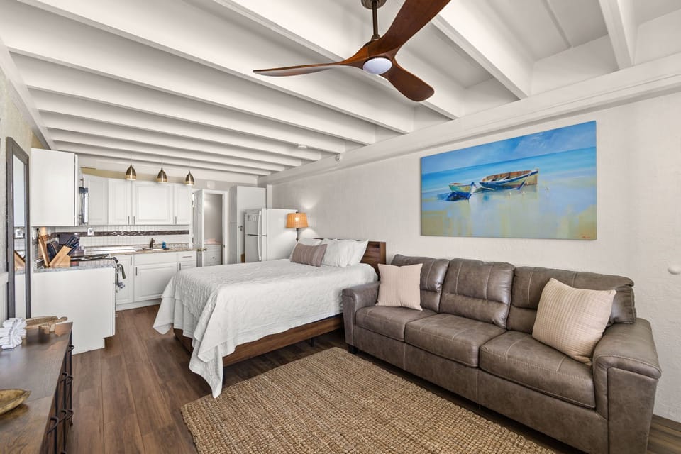 Inviting open-concept studio with coastal charm. Bright beamed ceilings, plush bed, and cozy sofa create the perfect retreat after a day of adventure.