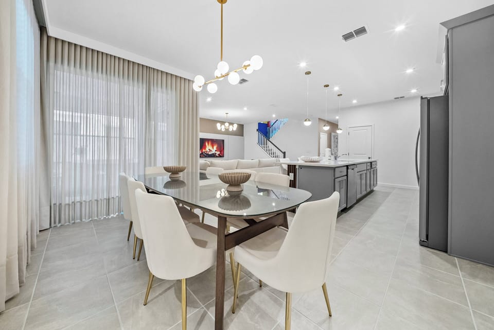 Enjoy the bright and airy dining area with a sleek glass table and plush white chairs, ideal for meals and conversations. Soft natural light streams through floor-to-ceiling curtains, creating a warm, inviting atmosphere.