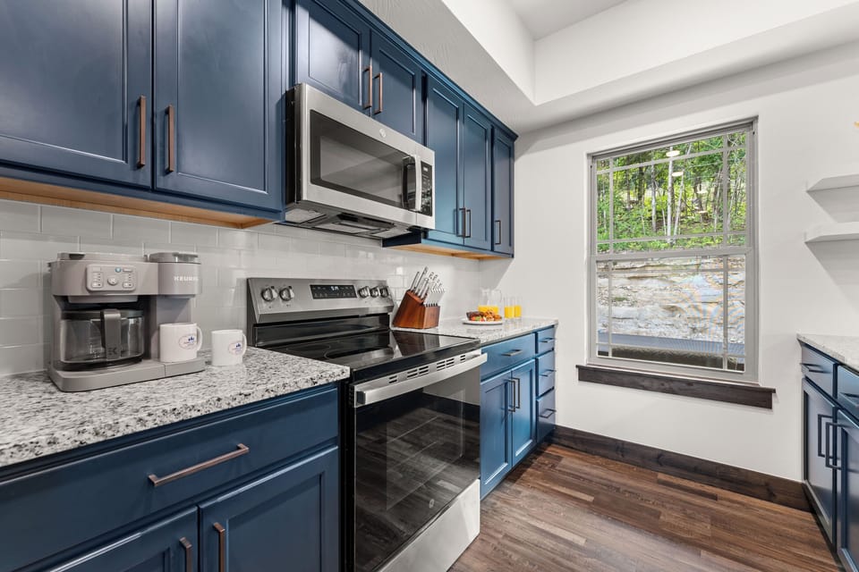 The fully equipped navy kitchen has granite counters, stainless appliances, a coffee bar, and a creekside window.