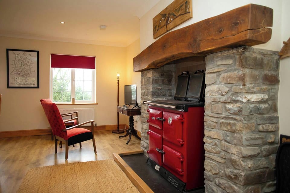 Red stove set into stone hearth with thick wooden mantel