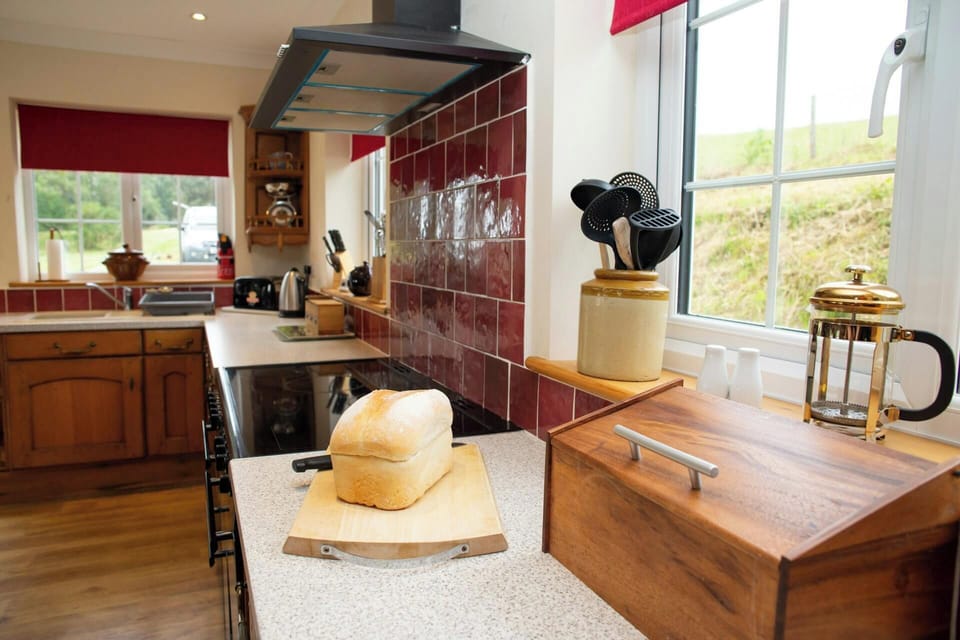 Kitchen worktop with loaf of bread, wooden bread bin and utensils by a window