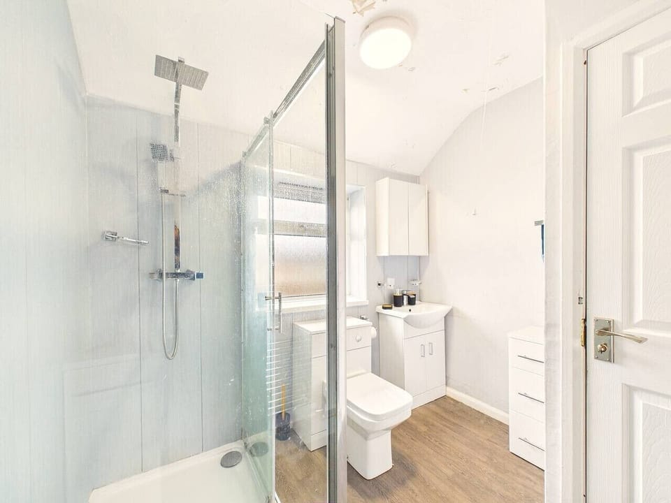 Enjoy a clean, functional layout with light blue paneled walls, stylish wood-effect flooring, and plenty of natural light from the frosted privacy window.