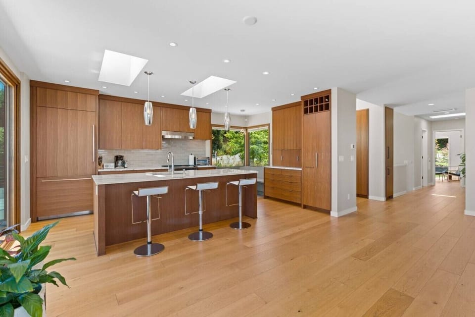 Skylit walnut kitchen with waterfall island, open to wide-plank oak floors.
